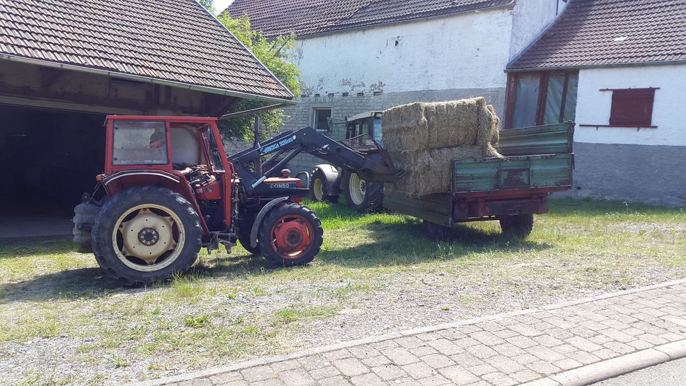 Heuballen werden vor der Scheune vom Anhänger geladen.