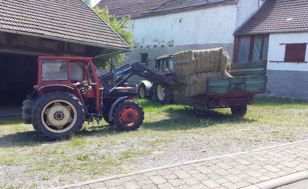 Heuballen werden vor der Scheune vom Anhänger geladen.