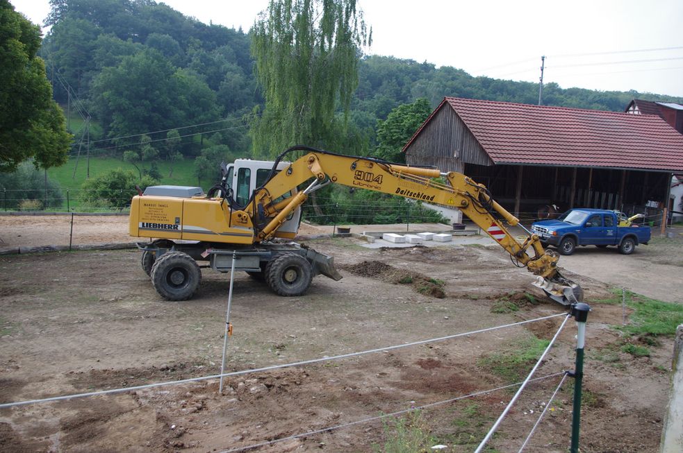 Bagger mit ausgestrecktem Schaufelarm ebnet den Boden für den Reitplatz